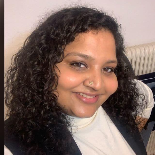 Close-up of a smiling woman with curly hair and a decorative nose stud.